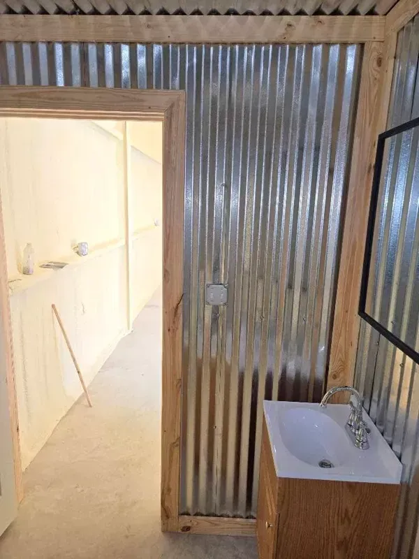 Small bathroom with corrugated metal walls, a sink, and a doorway opening to a bright adjacent room.