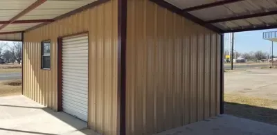 Brown metal-sided shed with a white roll-up door in a covered outdoor area