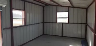 Empty metal-paneled room with two windows and a gray floor inside a small building
