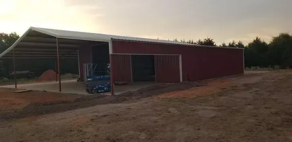 Red barn with open-sided shed and tractor at sunset on a dirt lot