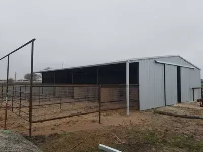 Small gray metal barn or shed in a fenced dirt field under an overcast sky