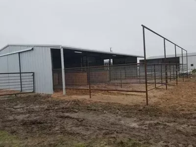 Metal barn and fenced livestock pens on a muddy rural property under an overcast sky