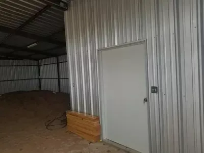 Empty metal barn interior with a white door and stacked wooden boards beside it