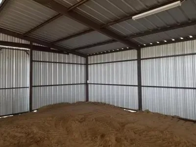 Empty corrugated metal shed with a dirt floor and exposed roof beams