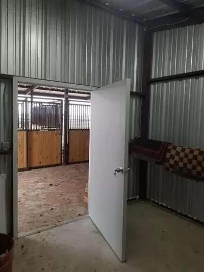 Open white door in a corrugated metal shed, showing a bare room with tiled floor and wood-paneled enclosure.