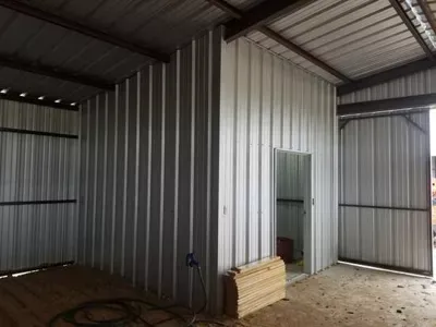 Empty corrugated metal shed interior with concrete floor and a small stack of boards by a doorway