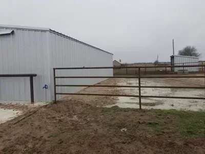 White metal barn beside a muddy fenced paddock under an overcast sky