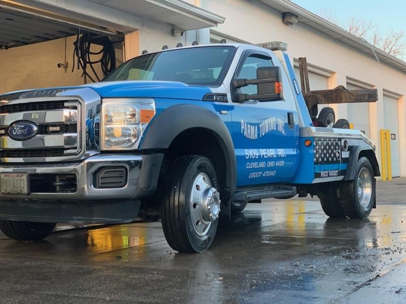 A blue and white tow truck is parked in front of a garage.