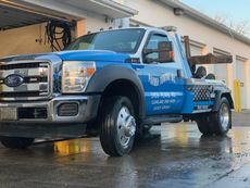 A blue and white tow truck is parked in front of a garage.