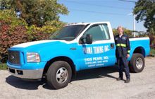 A man is standing next to a blue and white towing truck