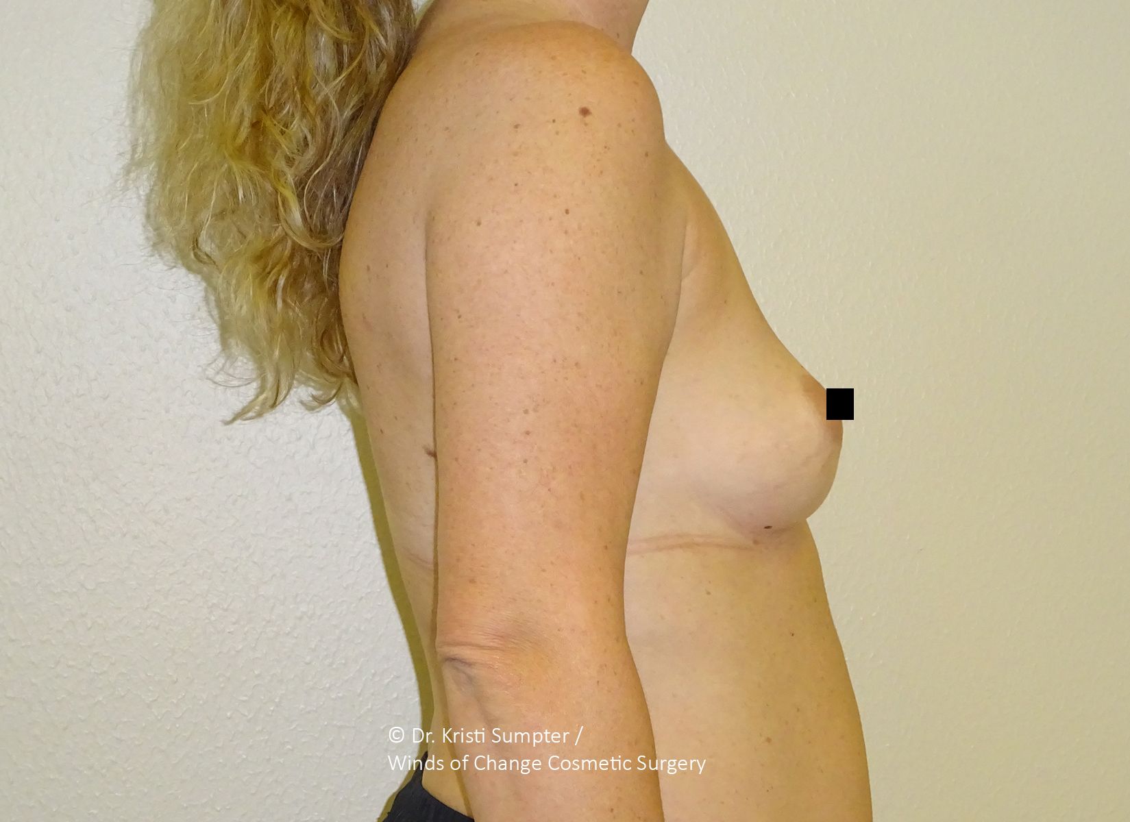 Side view of a person standing topless against a plain wall