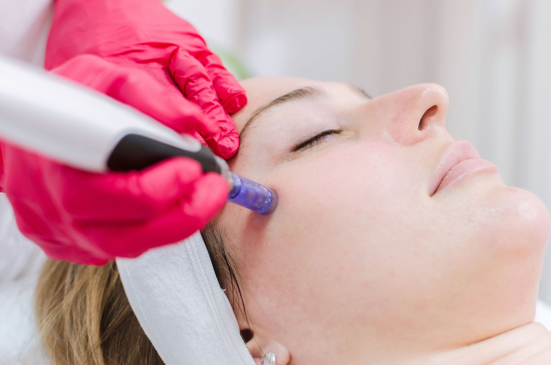 Gloved hands are using a blue facial treatment device on a woman’s face in a spa setting.