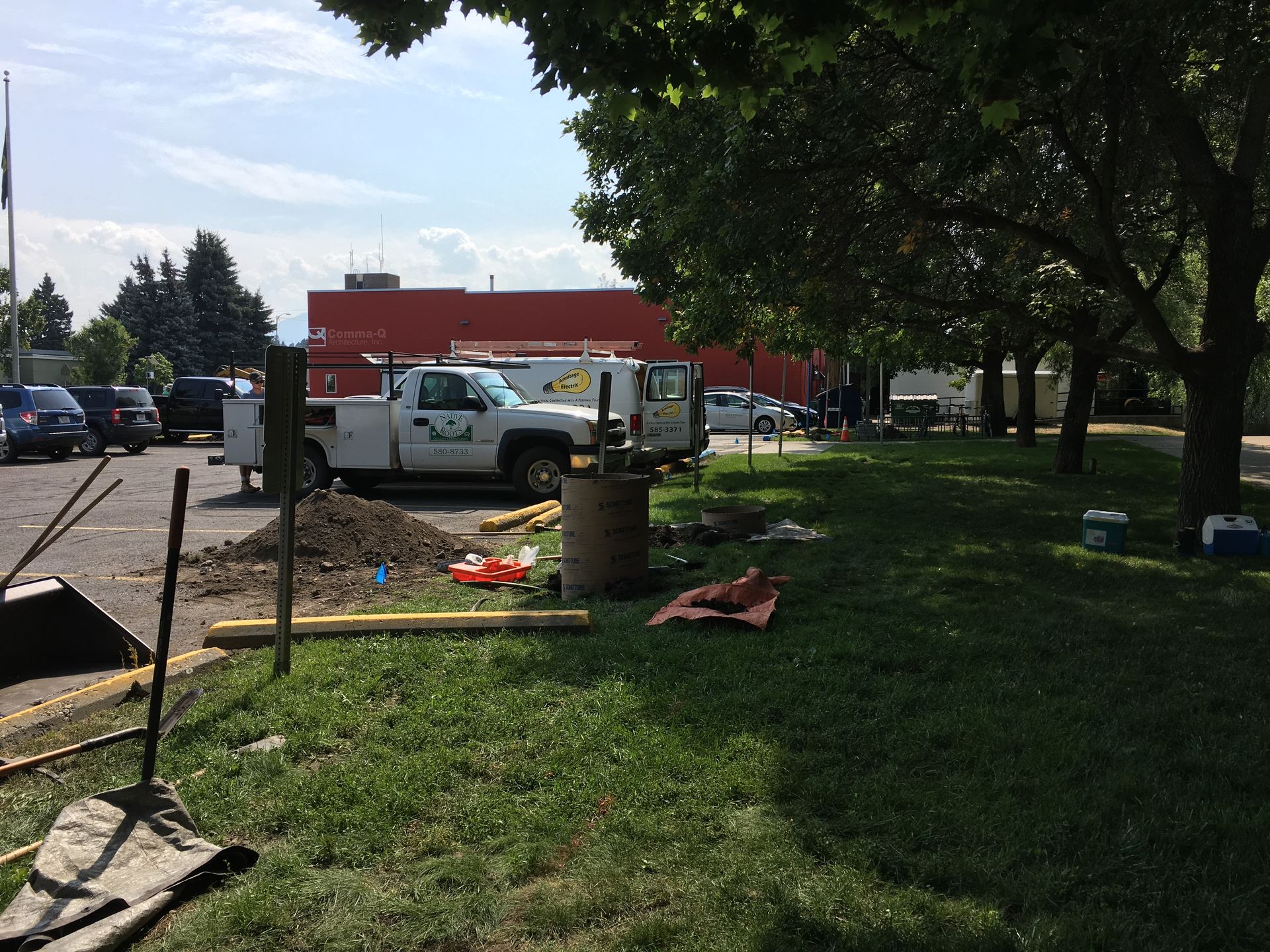 A utility truck parked at a construction site with a dirt pile and equipment on a grassy verge near a building.
