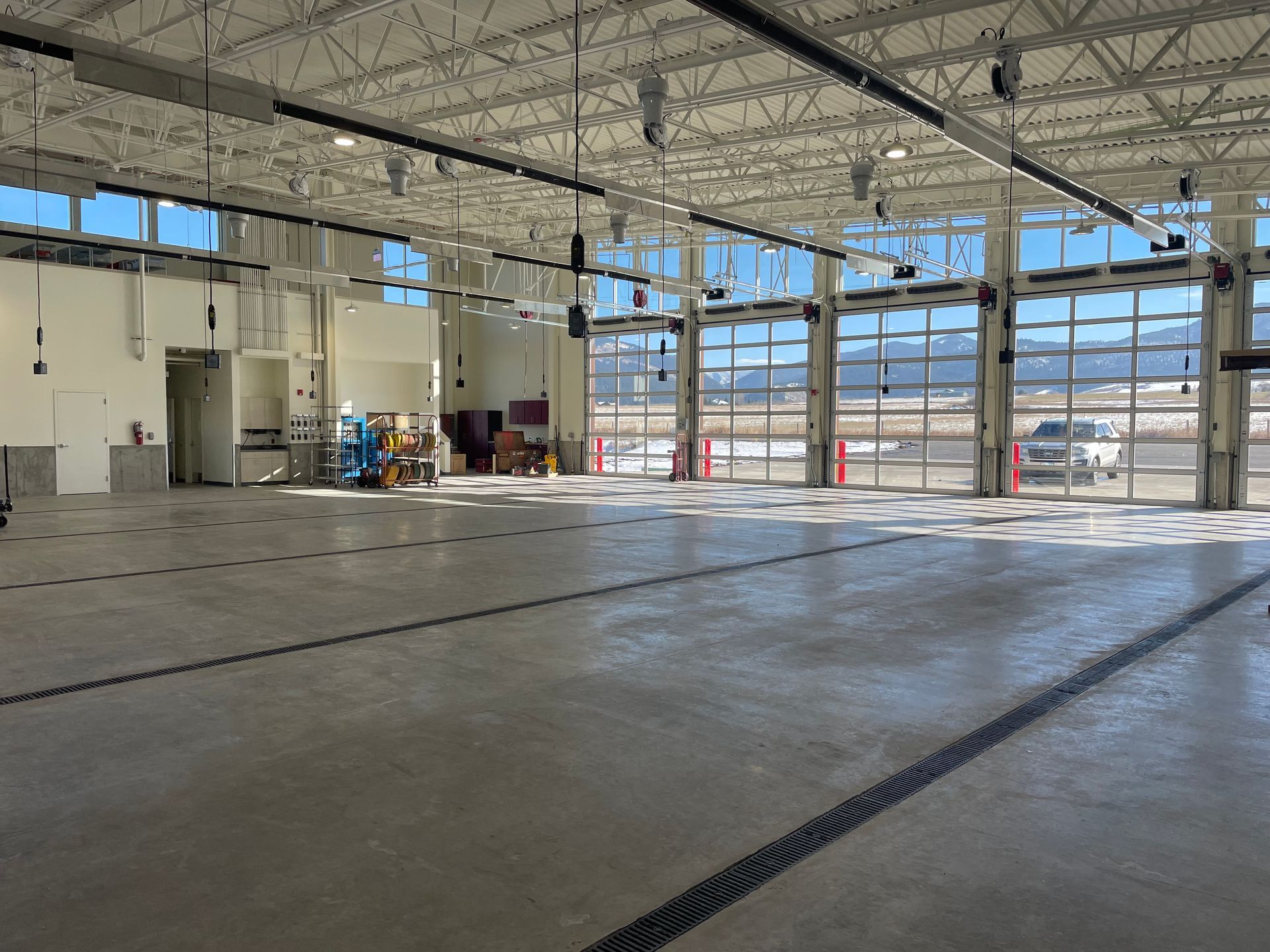 An empty, expansive industrial garage or fire station with a concrete floor, high ceilings, and large glass bay doors.