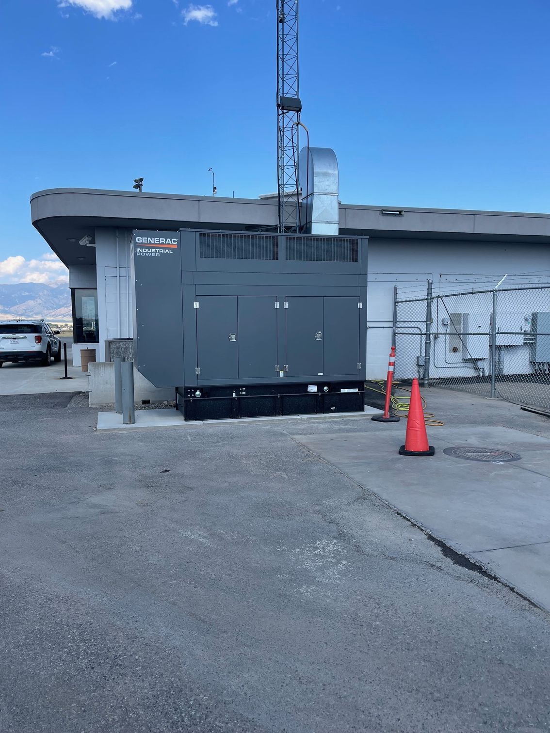 A large, gray backup generator sits on a concrete pad outside a building under a clear blue sky.