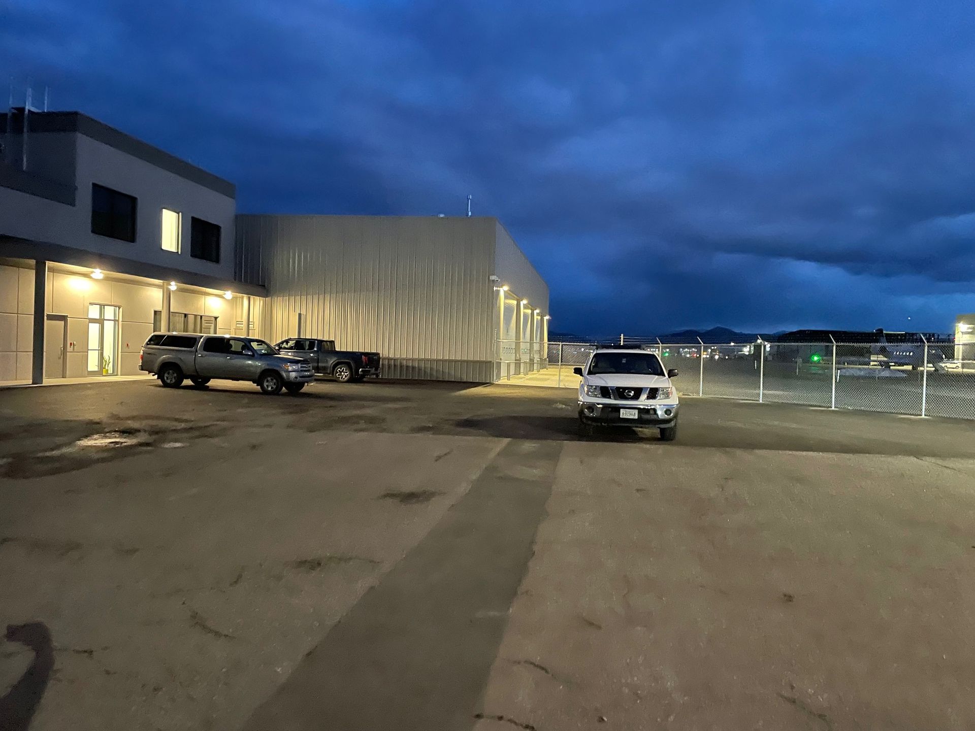 A building exterior with two parked pickup trucks at twilight under a cloudy blue sky.