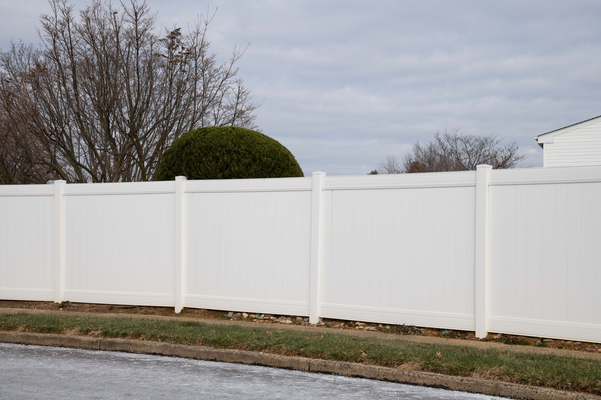 White vinyl fence along a roadside with bare trees and a cloudy sky