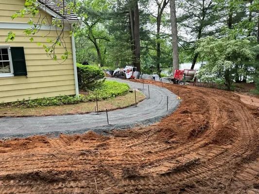 A curving gravel path under construction next to a yellow house with dark shutters, surrounded by dirt and trees.