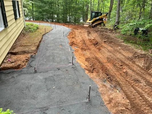 A construction scene shows a graded dirt path lined with stakes and black fabric next to a yellow house and a skid steer.