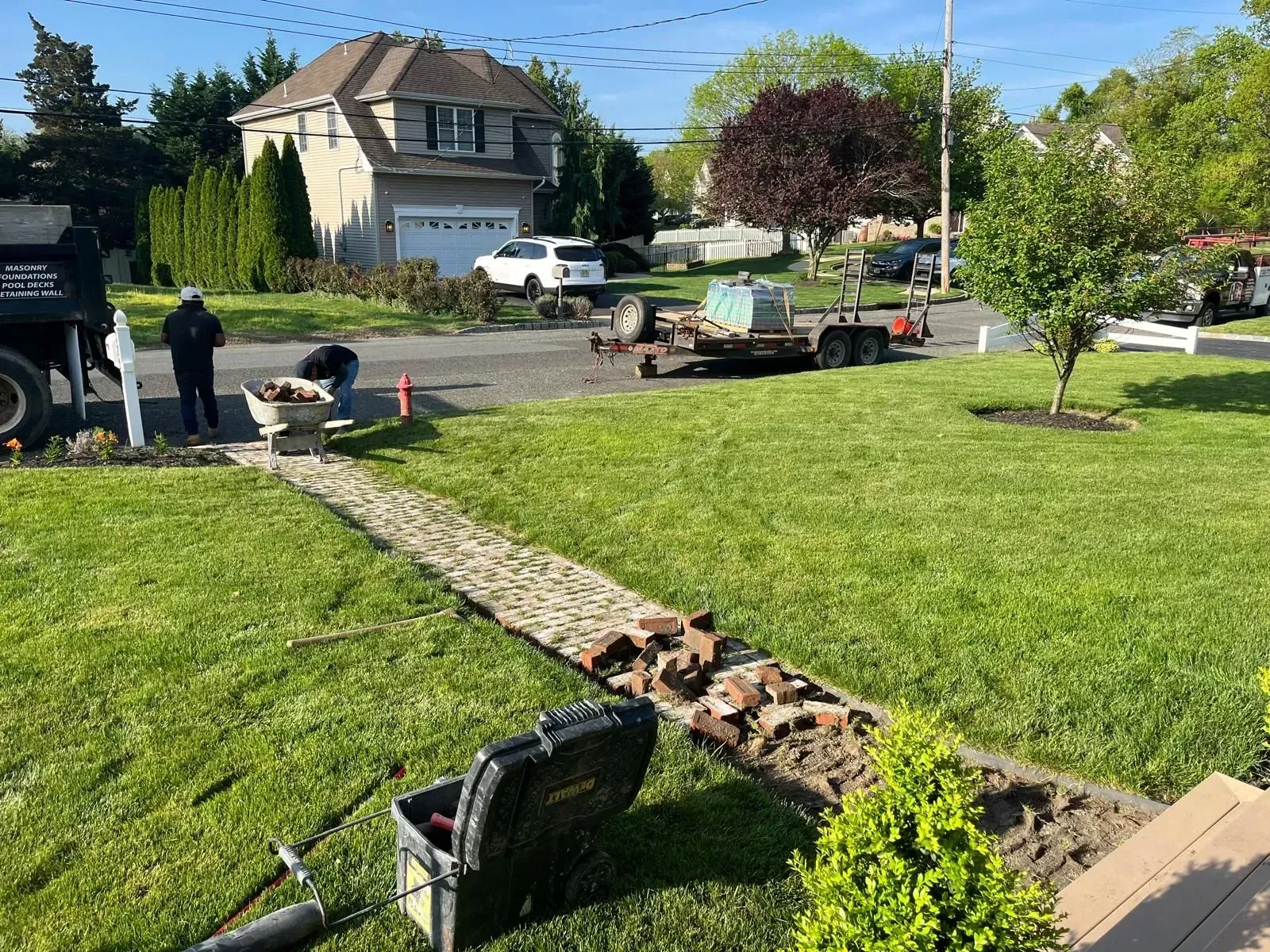 Workers installing a stone walkway on a sunny day in a residential neighborhood.