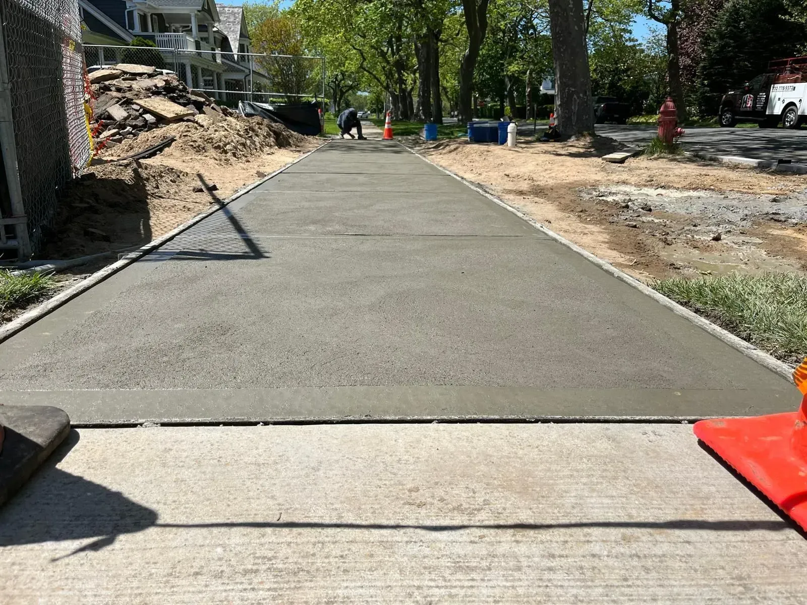 A freshly poured, smooth gray concrete sidewalk section under construction in a tree-lined residential neighborhood.