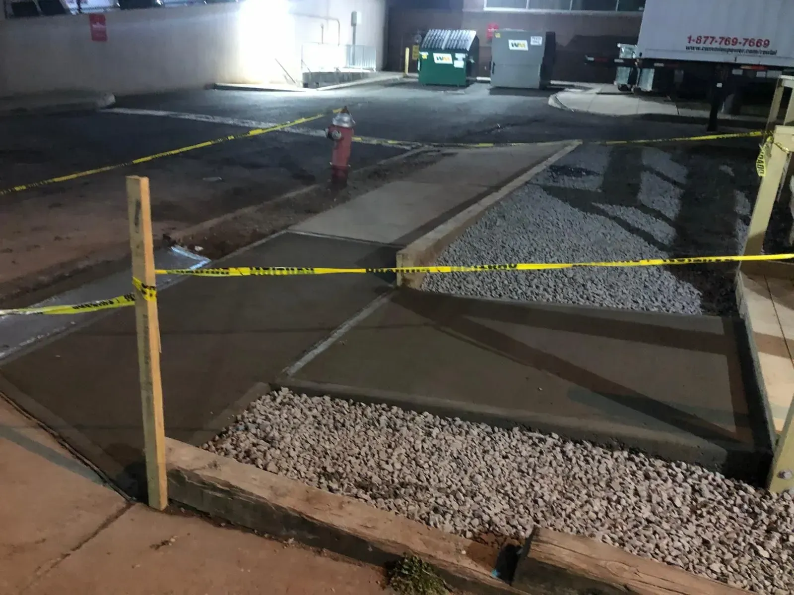Newly poured concrete sidewalk sections in an outdoor parking area cordoned off by yellow caution tape at night.