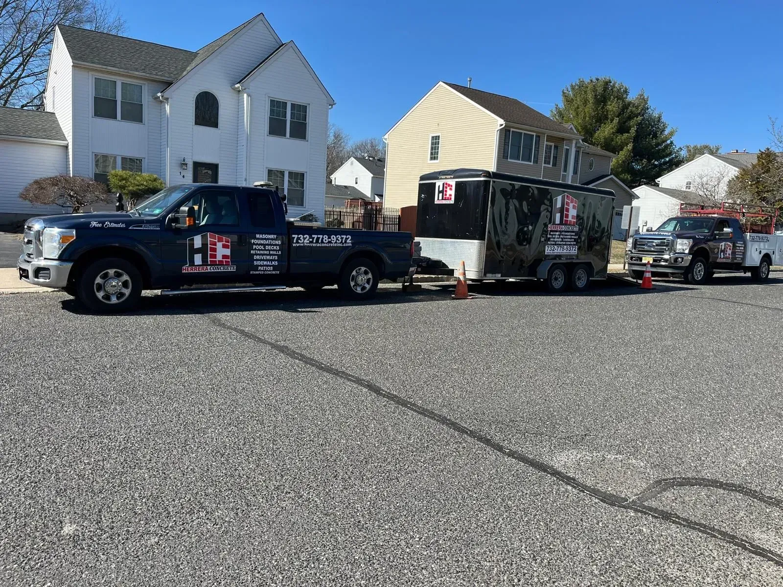 Two dark-colored service trucks and an enclosed trailer parked on a gravel surface in a residential neighborhood.