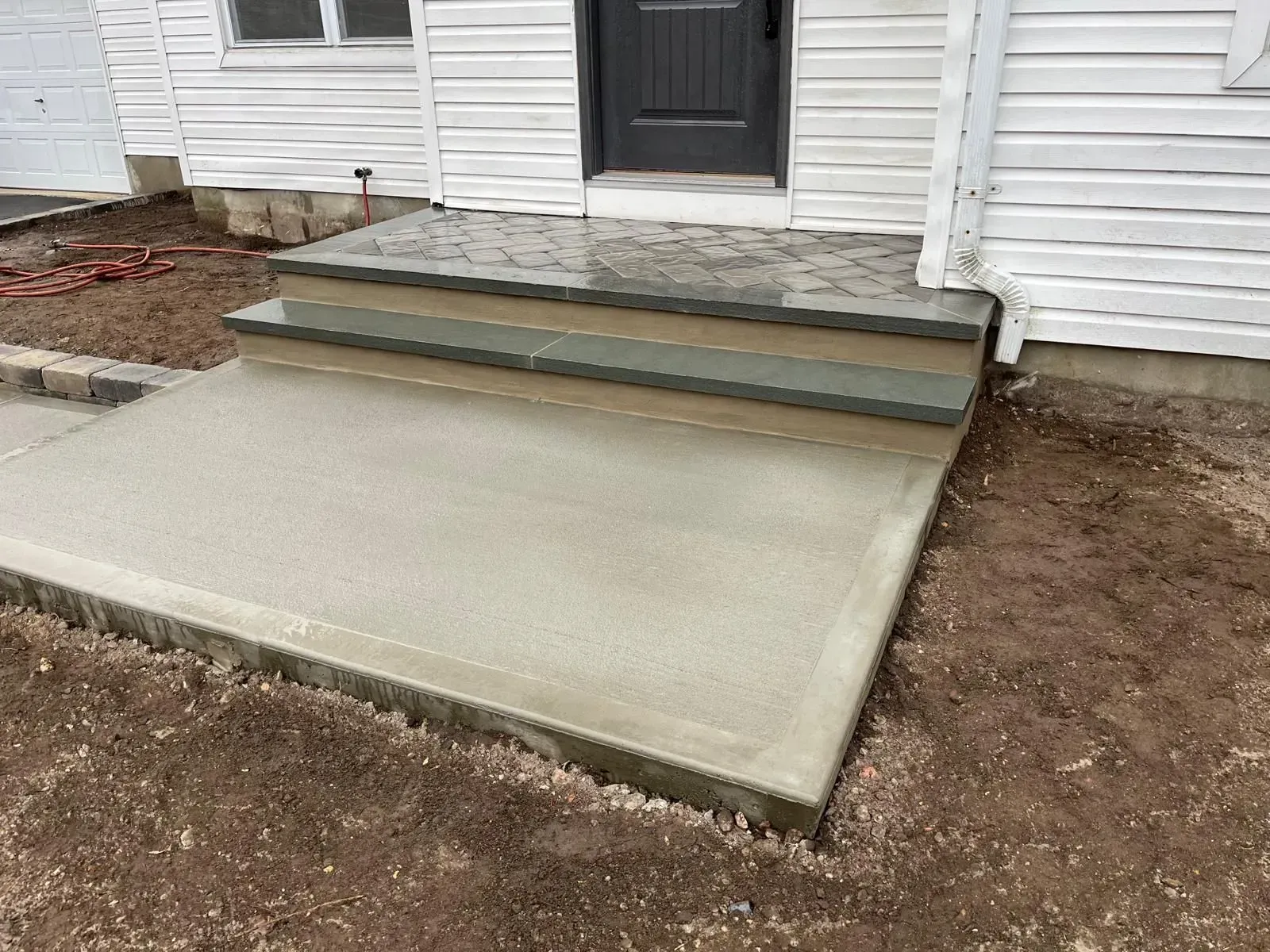 A newly poured concrete landing with two matching steps leading to a white-sided house with a black front door.