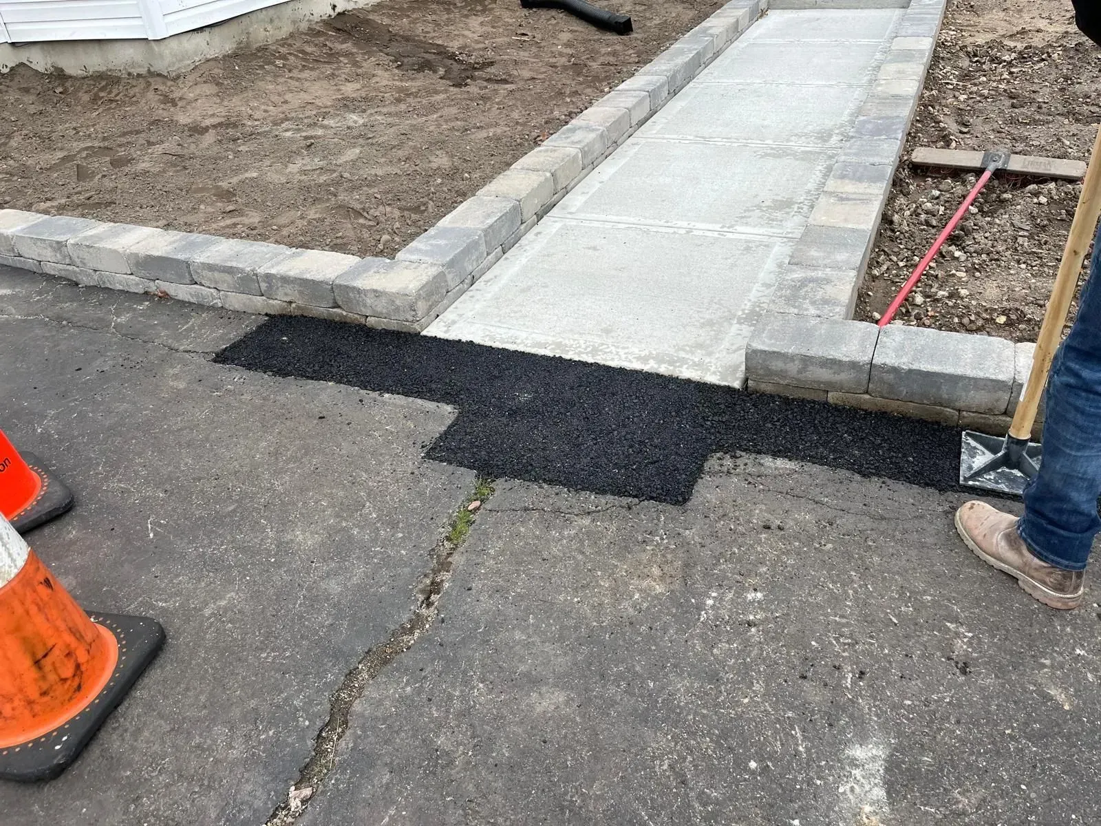 A new asphalt patch connects a paved driveway to a concrete walkway flanked by gray stone edging.