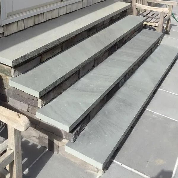 A stone staircase with four broad, smooth, light-gray steps leading up to a doorway on a patio.