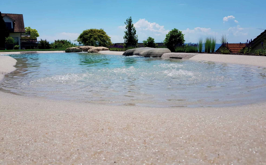 A natural swimming pool with clear water, light-colored edge, rocks, and blue sky.