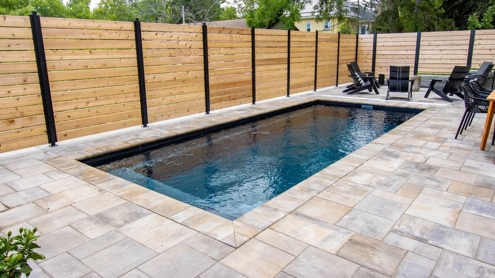 A large swimming pool is surrounded by a wooden fence and chairs.