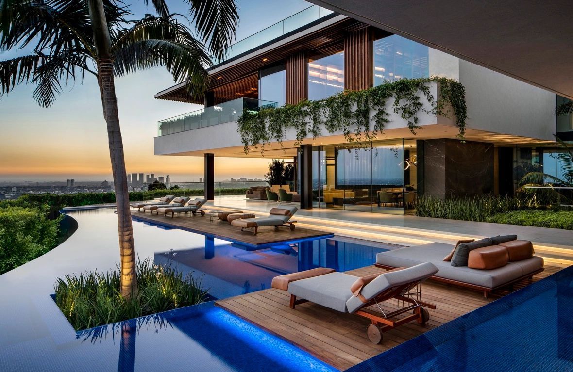 A large house with a swimming pool and lounge chairs in front of it.