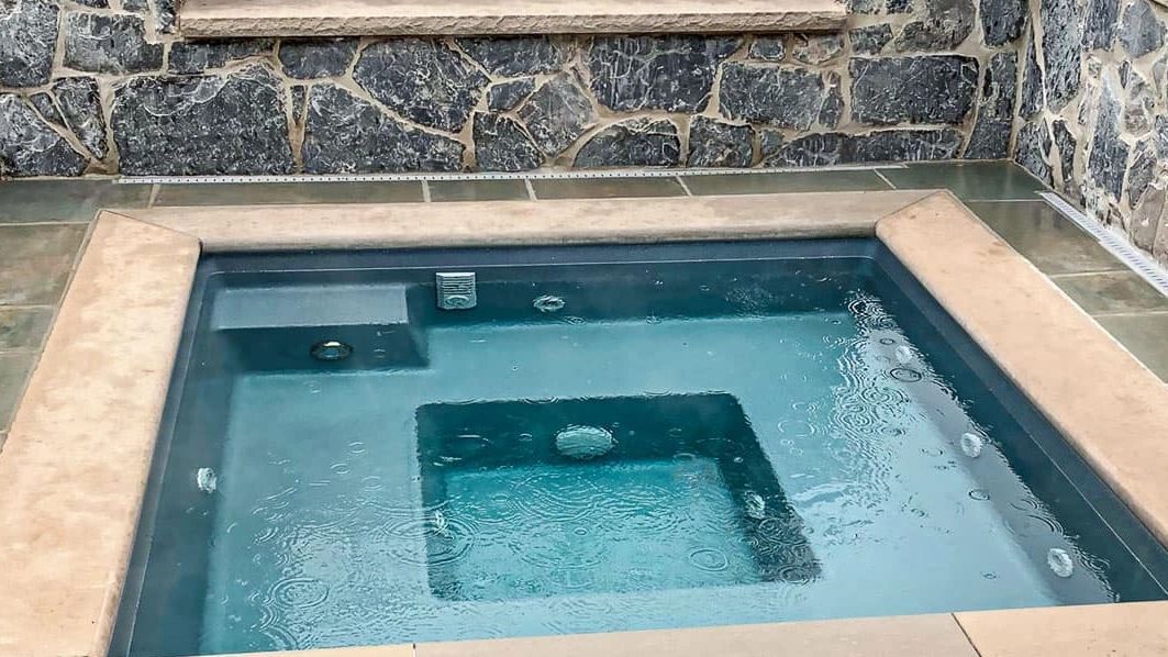A square hot tub is surrounded by a stone wall.