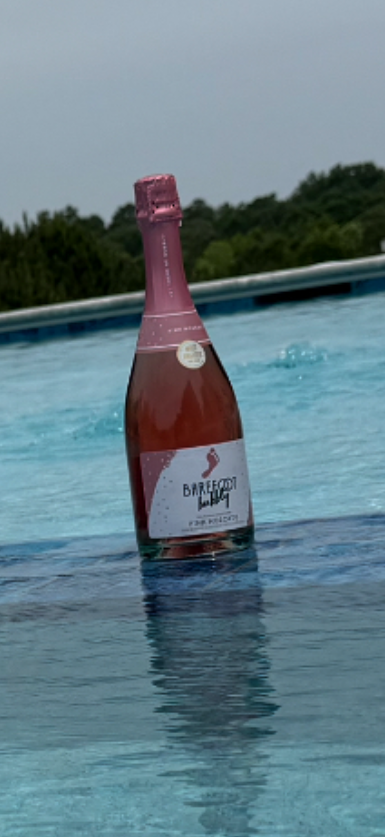 A bottle of Barefoot Bubbly rosé in a pool with trees in the background.