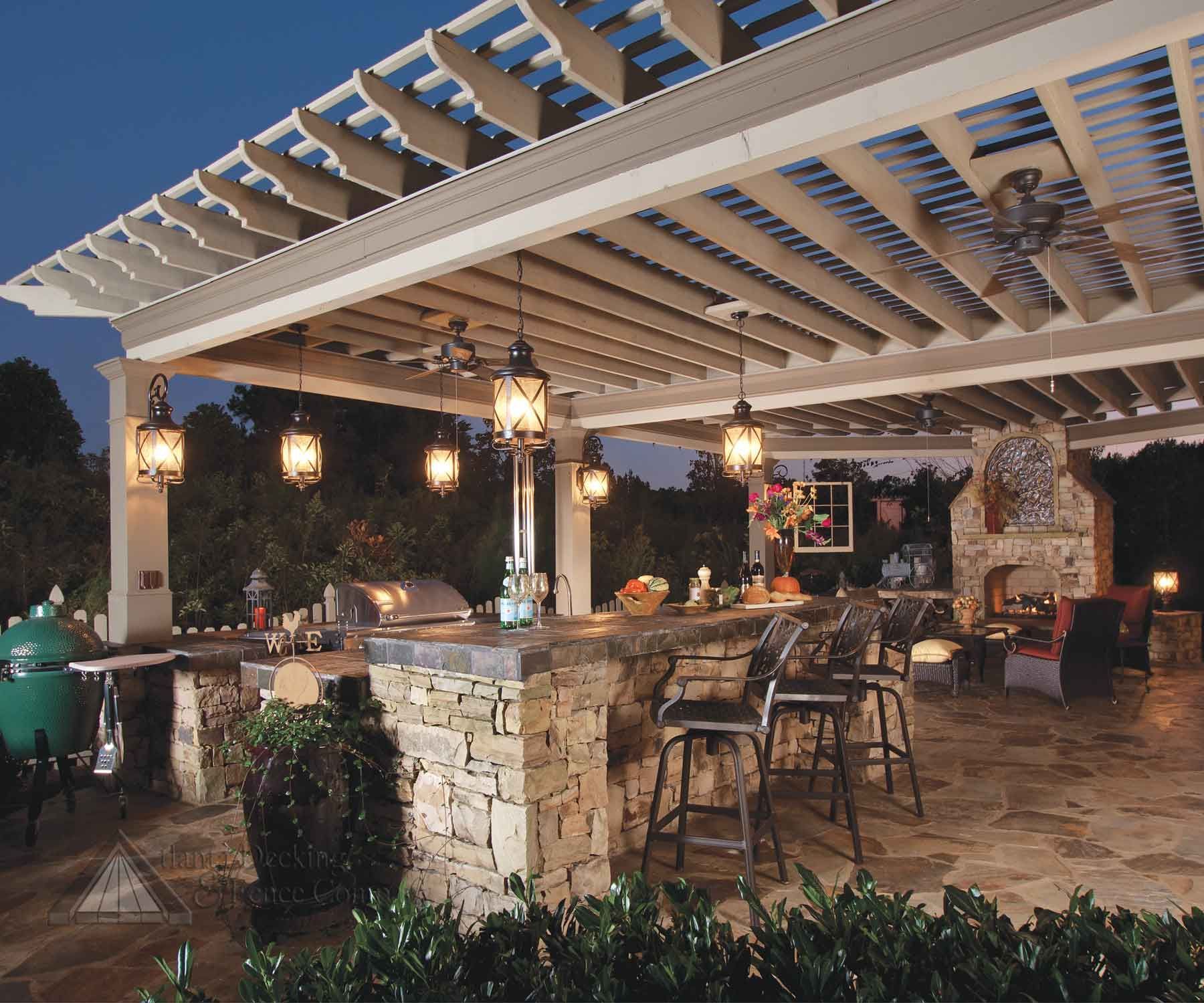 Outdoor kitchen with stone bar, pergola, fireplace, and hanging lights.