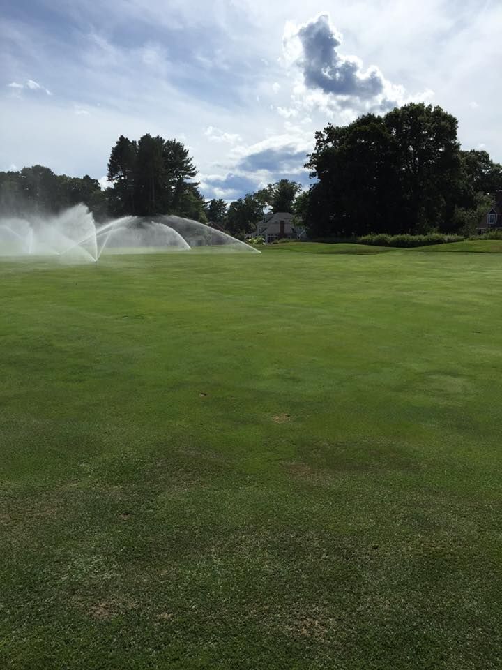 A golf course with sprinklers spraying water on the grass.