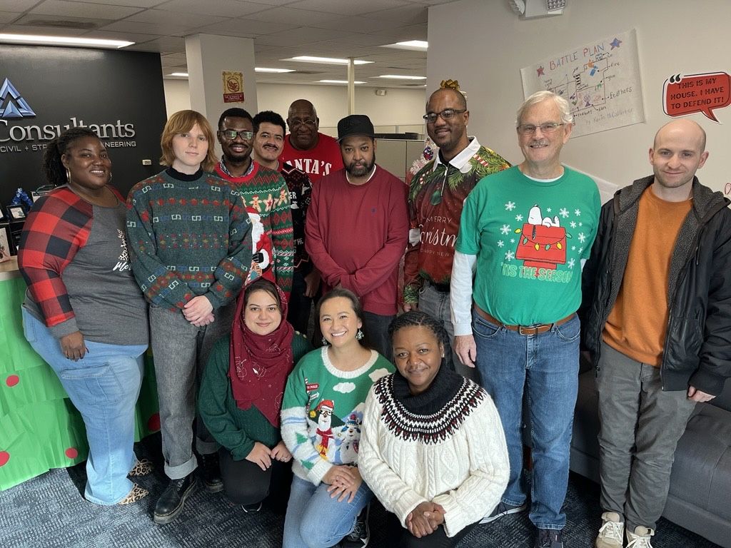 Group of people in Christmas sweaters posing for a photo in an office setting.