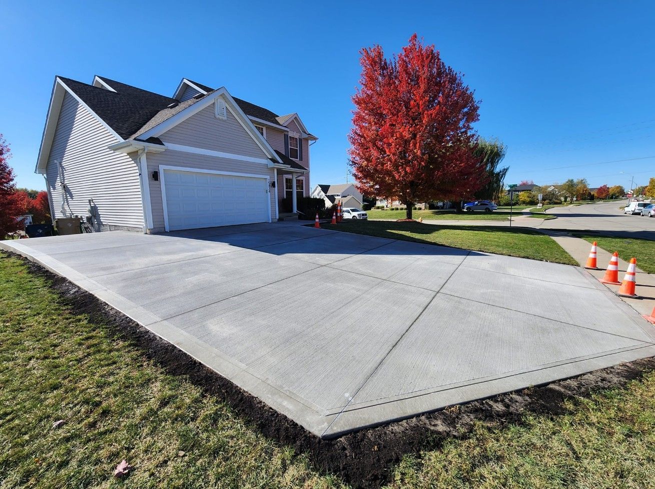 A light-colored house with a two-car garage and a newly poured, expansive concrete driveway on a sunny, autumn day.