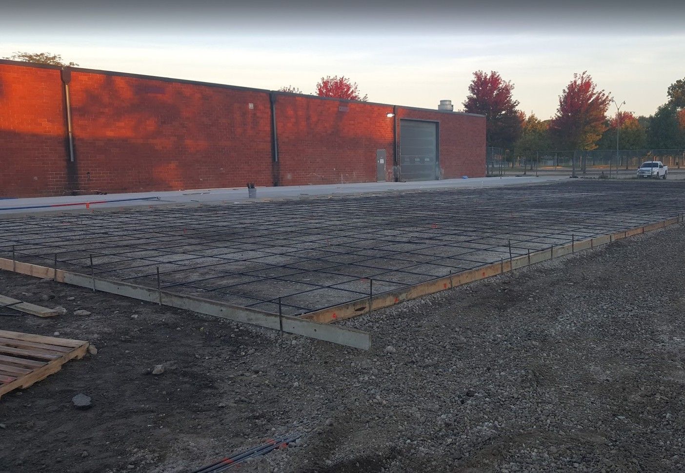 Construction site with gravel, wooden frame, and red brick wall in the background.