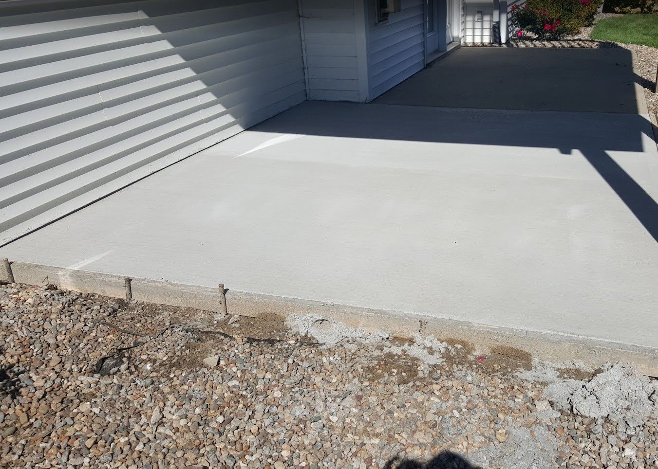 A newly poured concrete patio next to a house with white siding and gravel.