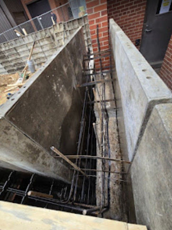 Construction site with metal forms and steel rebar cage set up for a concrete foundation wall next to a brick building.