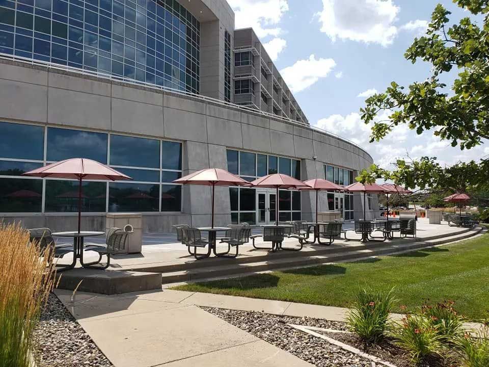 Outdoor patio with tables, umbrellas, and a large building in the background. Sunny day.