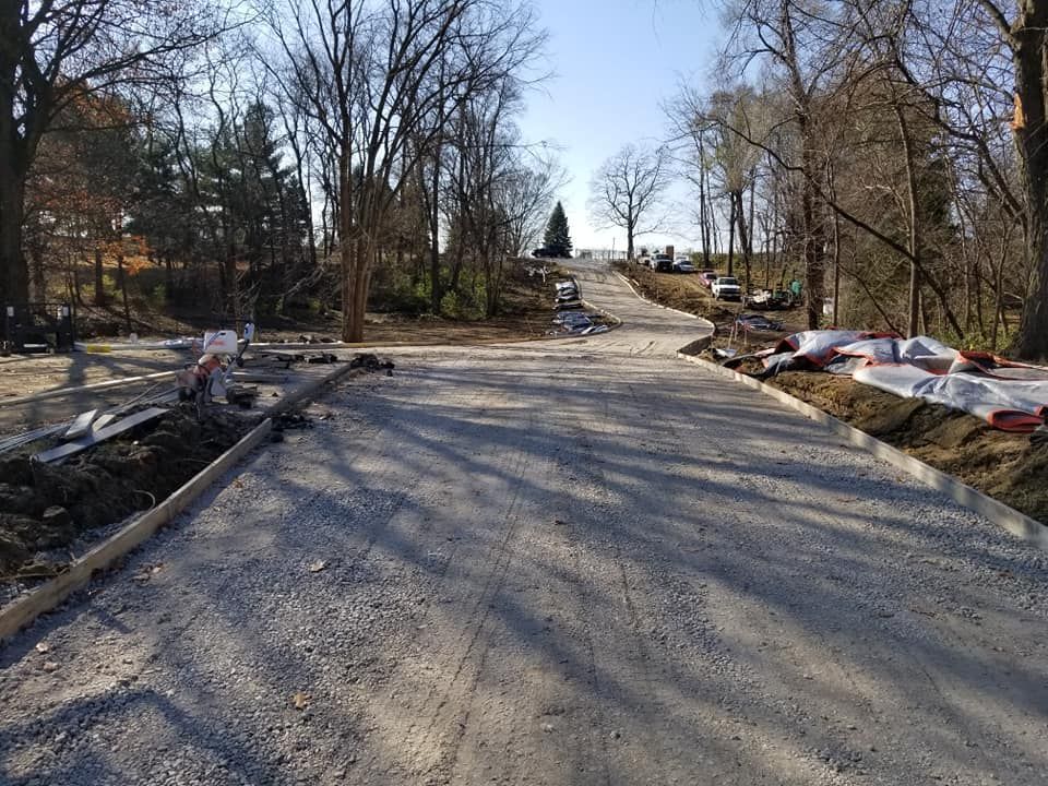 Gravel road construction in a wooded area; trees on either side.