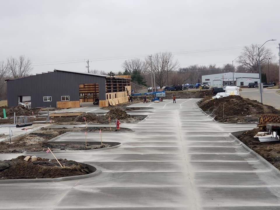 Construction site with new concrete parking lot. Building frame visible, overcast sky.