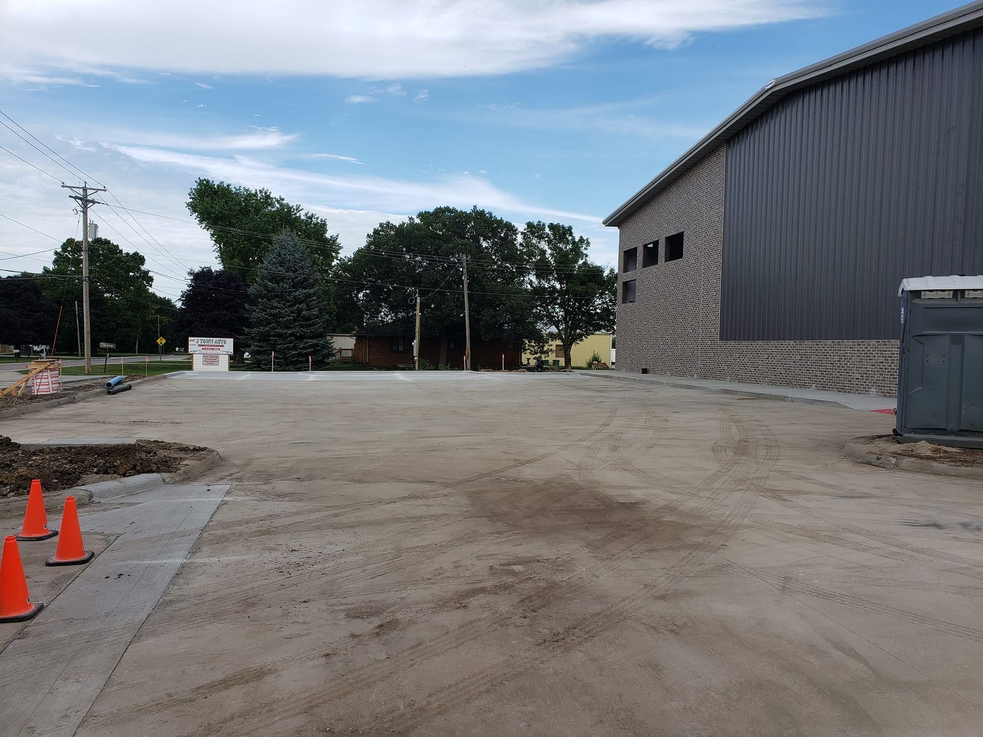 Gravel lot beside a gray building, with trees and power lines in the background under a cloudy sky.