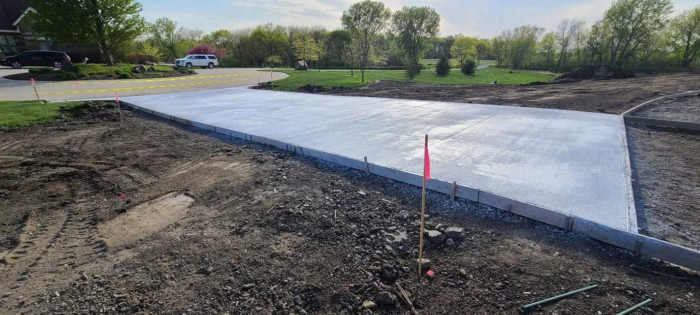 Newly poured concrete driveway with surrounding dirt and grass, trees in the background.