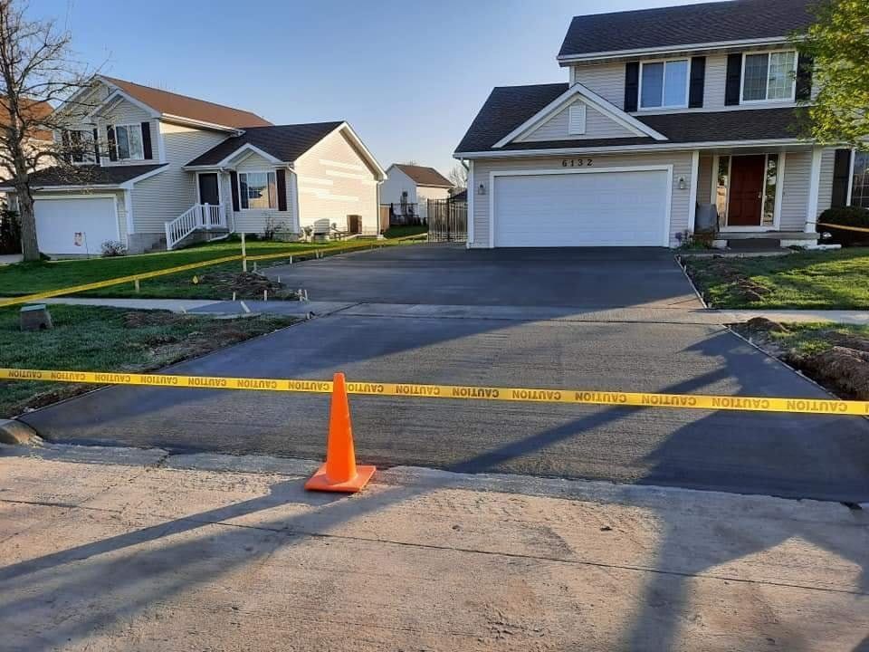 A newly paved driveway with caution tape and traffic cone, in front of two suburban homes.
