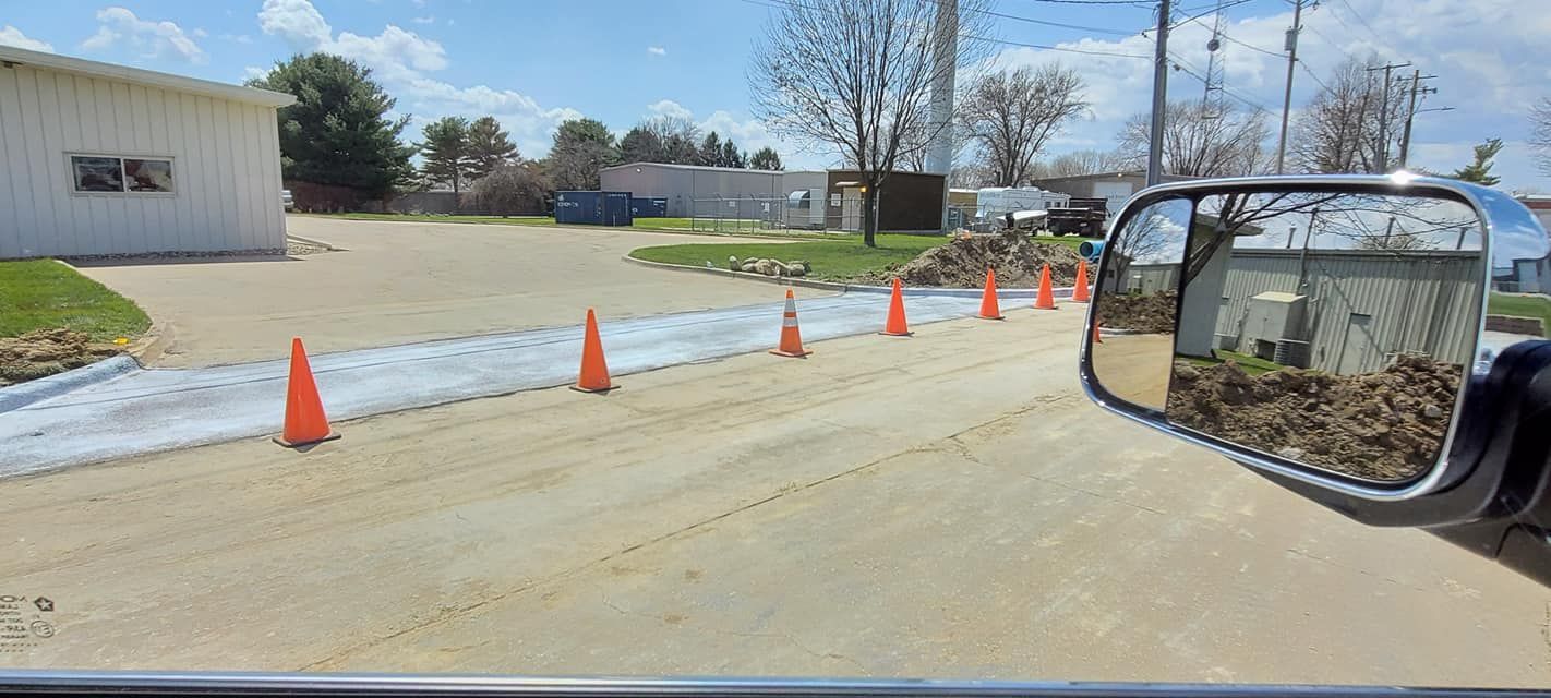 Orange cones line a dirt road in front of a white building, seen from a vehicle's side mirror.