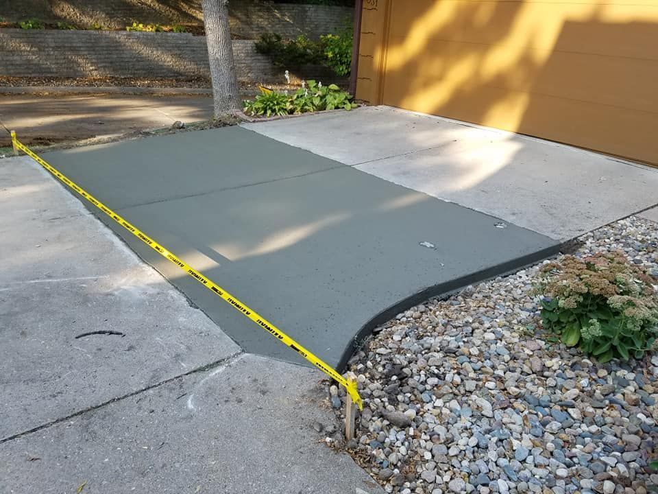Freshly poured concrete driveway section, bordered by gravel and yellow caution tape.